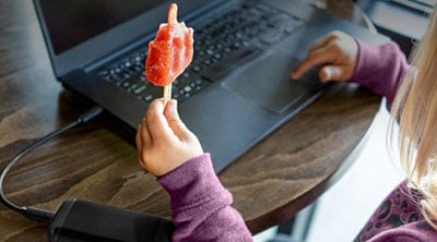 Child eating popsicle on laptop
