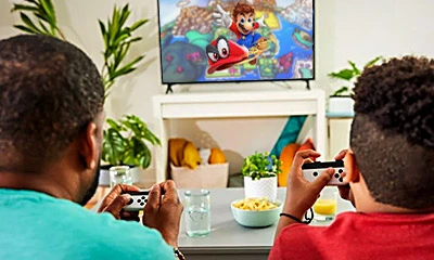 Father and son playing Super Mario Odyssey with Nintendo Switch on TV mode